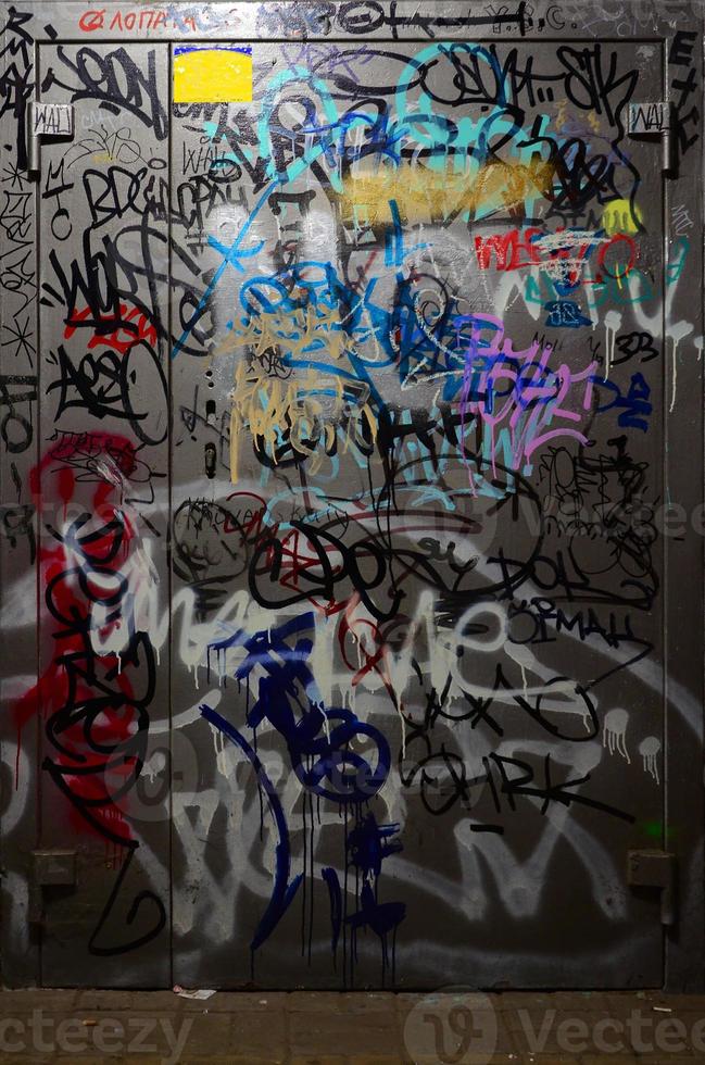 fragment av graffiti taggar. de gammal vägg är bortskämd med måla fläckar i de stil av gata konst kultur. målad metall dörr foto