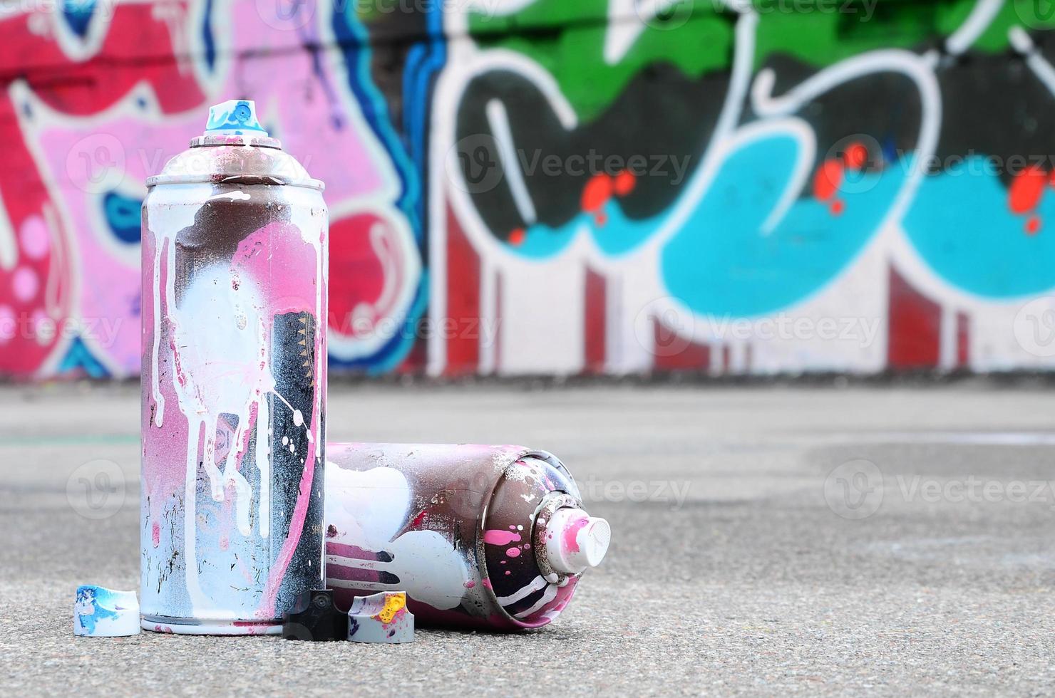 flera Begagnade spray burkar med rosa och vit måla och caps för besprutning måla under tryck är lögner på de asfalt nära de målad vägg i färgad graffiti ritningar foto