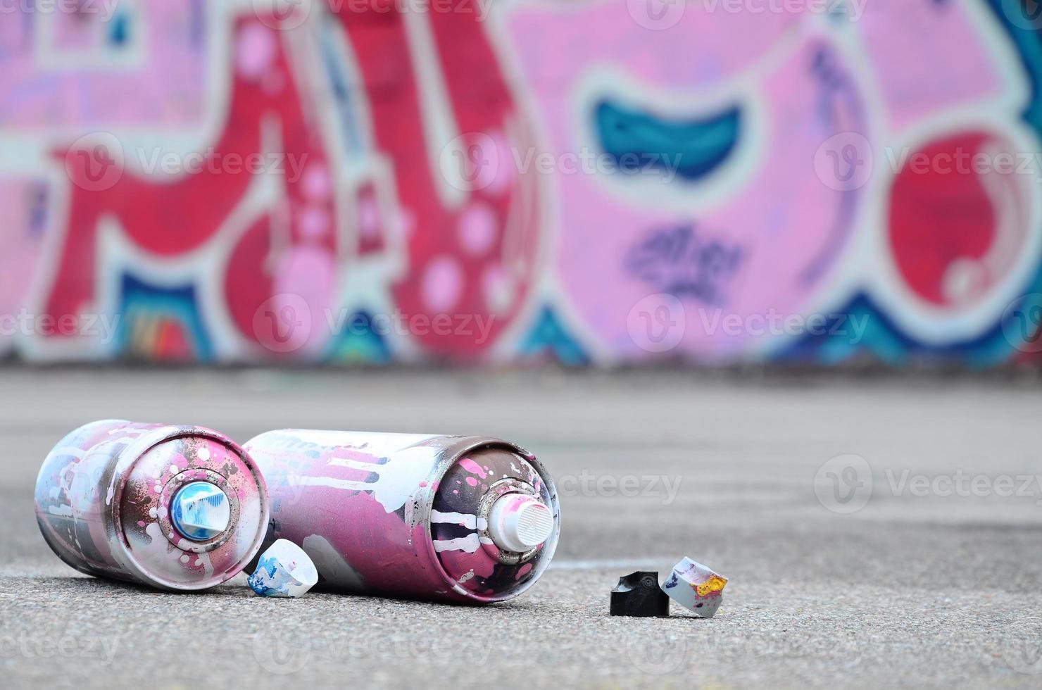 flera Begagnade spray burkar med rosa och vit måla och caps för besprutning måla under tryck är lögner på de asfalt nära de målad vägg i färgad graffiti ritningar foto