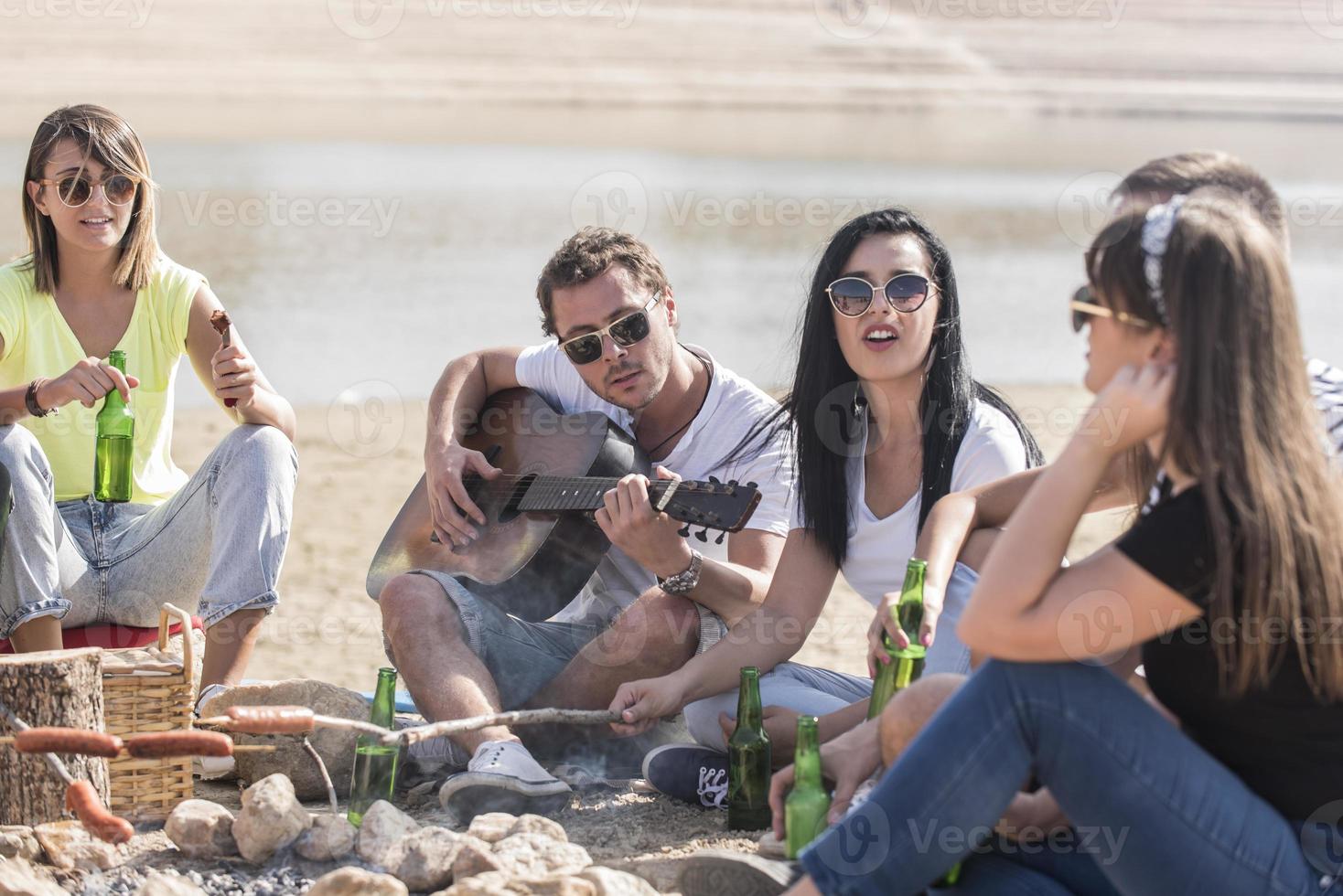 Lycklig vänner camping fest spelar musik och njuter bål i natur och sjö, foto