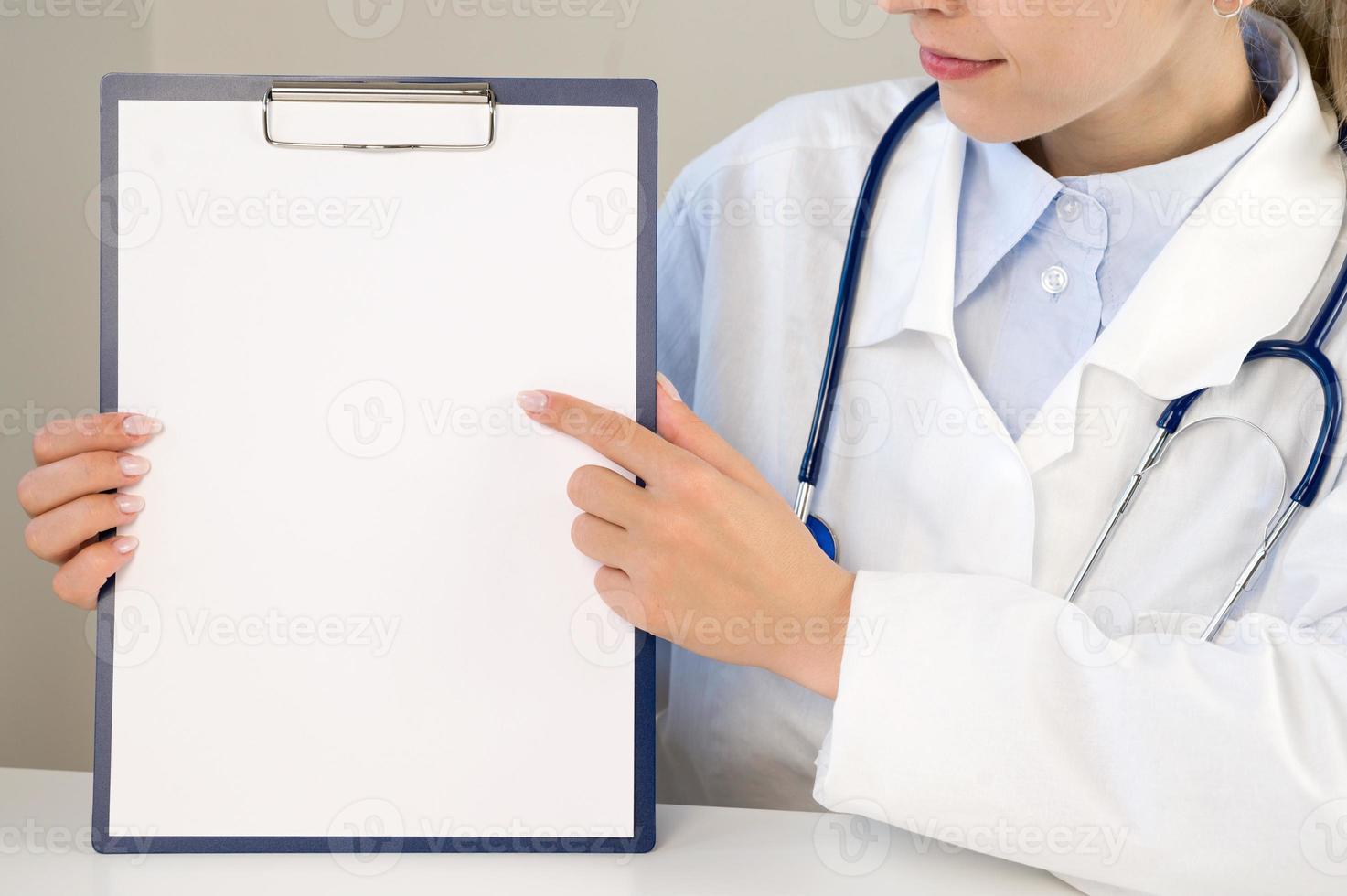 en läkare i en vit täcka poäng till ett tömma Plats på en papper. de läkare är innehav en mapp med ett tömma ark i hans händer. Plats för kopia och uppgifter. medicinsk begrepp. foto