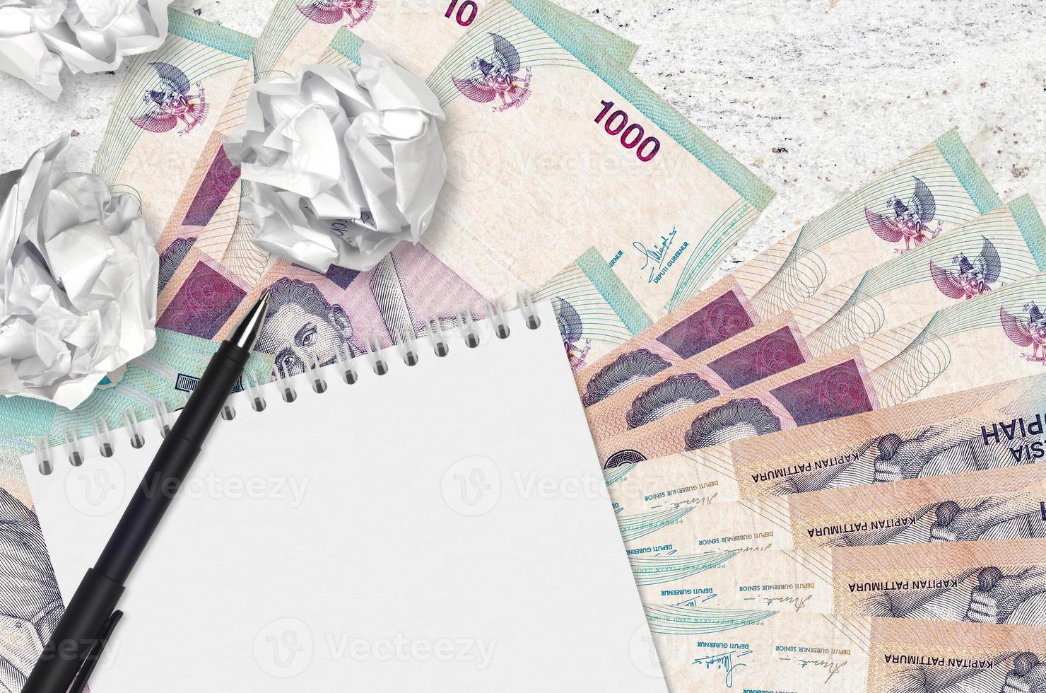 1000 indonesiska rupiah räkningar och bollar av skrynkliga papper med tom anteckningsblock. dålig idéer eller mindre av inspiration begrepp. sökande idéer för investering foto