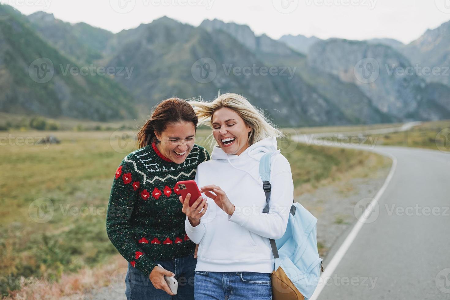 Lycklig ung kvinnor resenärer använder sig av mobil på väg mot de skön berg landskap foto