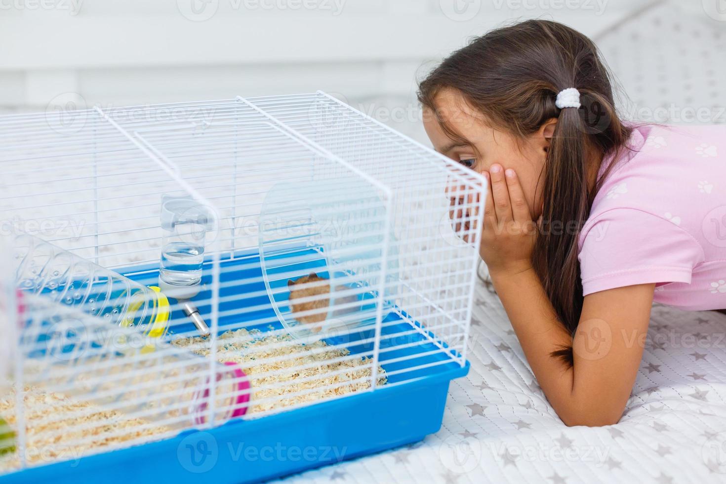 liten flicka innehar bur för hamster på Hem foto