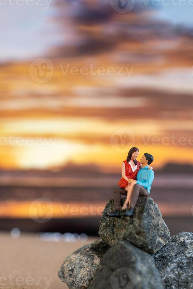 miniatyr- människor , par Sammanträde på en hav strand med solnedgång bakgrund foto