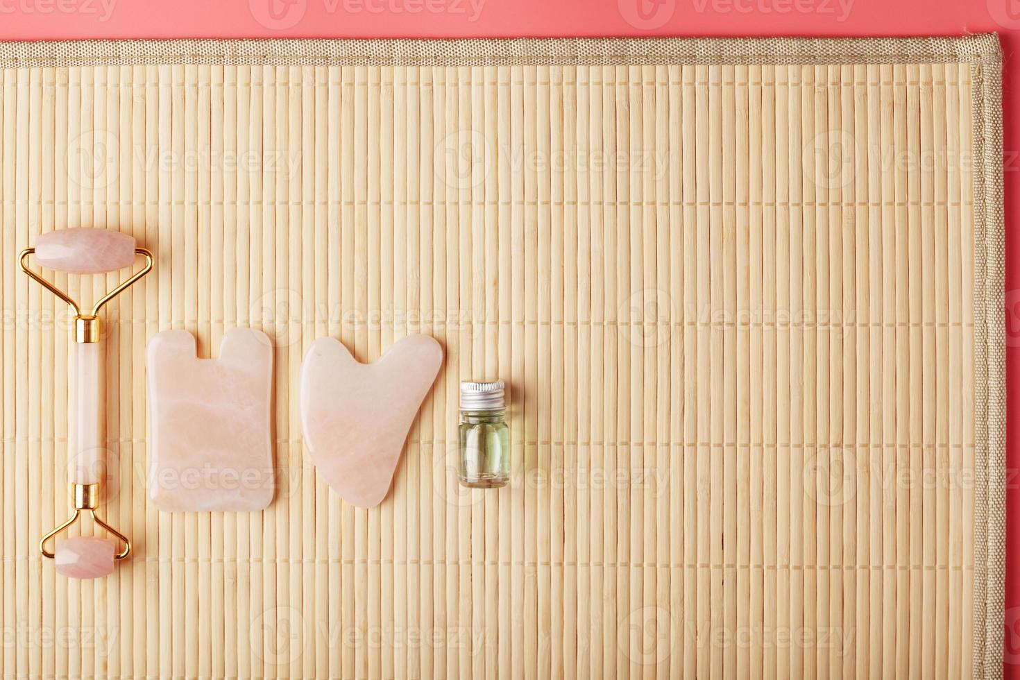 en uppsättning av verktyg för ansikte massage Metod gua sha tillverkad av naturlig reste sig kvarts. vält, jade sten och olja i en glas burk, på en sugrör bakgrund för ansikte och kropp vård. foto