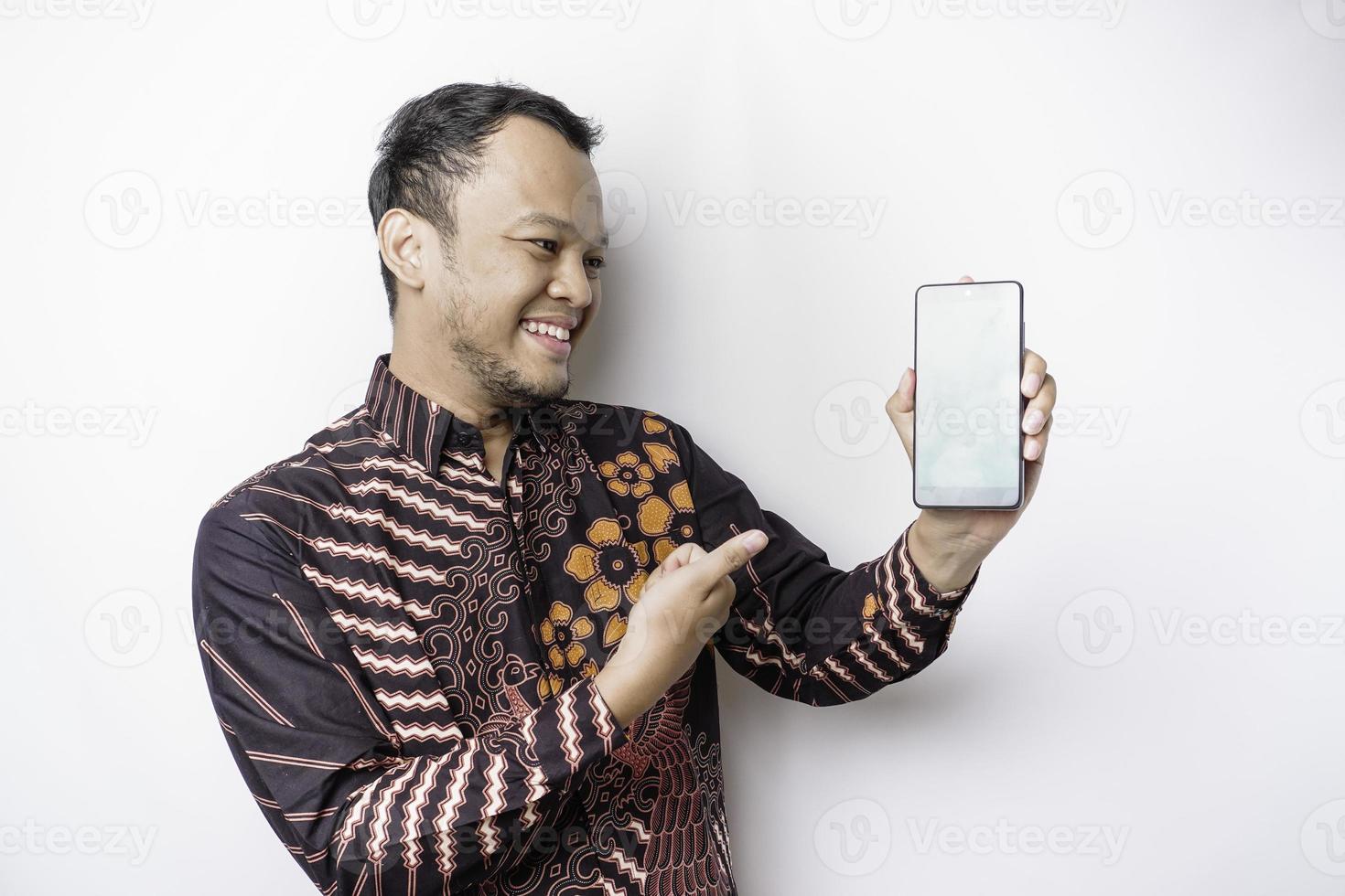 en porträtt av en leende asiatisk man bär en batik skjorta och som visar grön skärm på henne telefon, isolerat förbi vit bakgrund foto