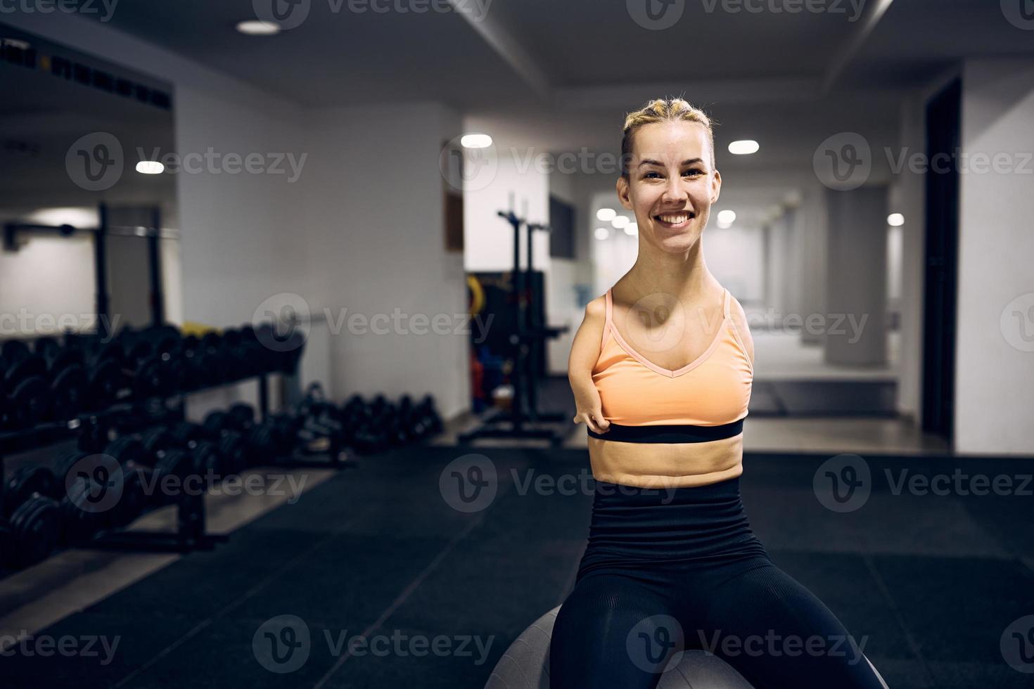 Lycklig armlös kvinna idrottare avkopplande på kondition boll i en Gym och ser på kamera. foto