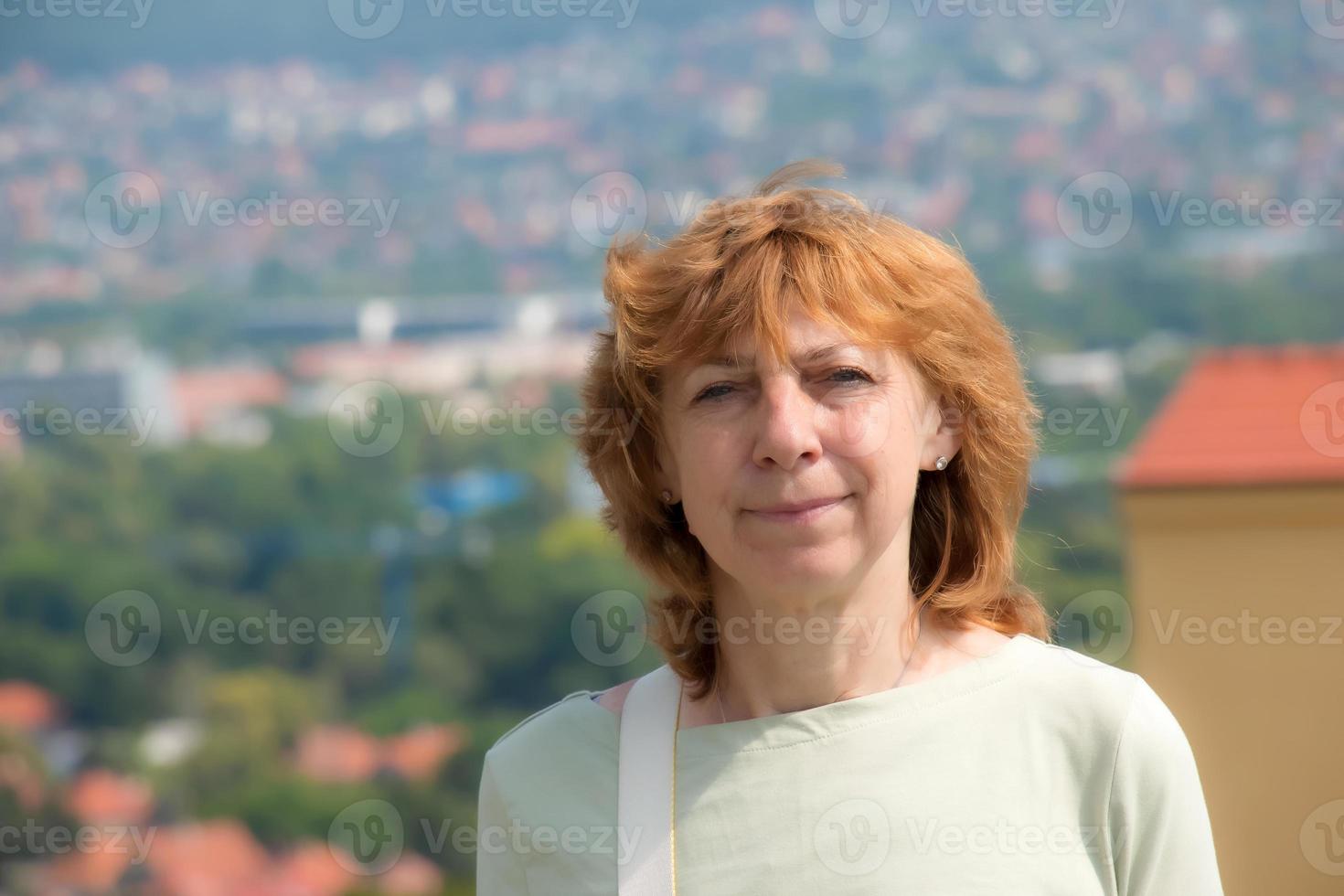 porträtt av en Söt åldrig kvinna mot de bakgrund av en typisk europeisk stad med röd tak. skön landskap med en suddig bakgrund. foto