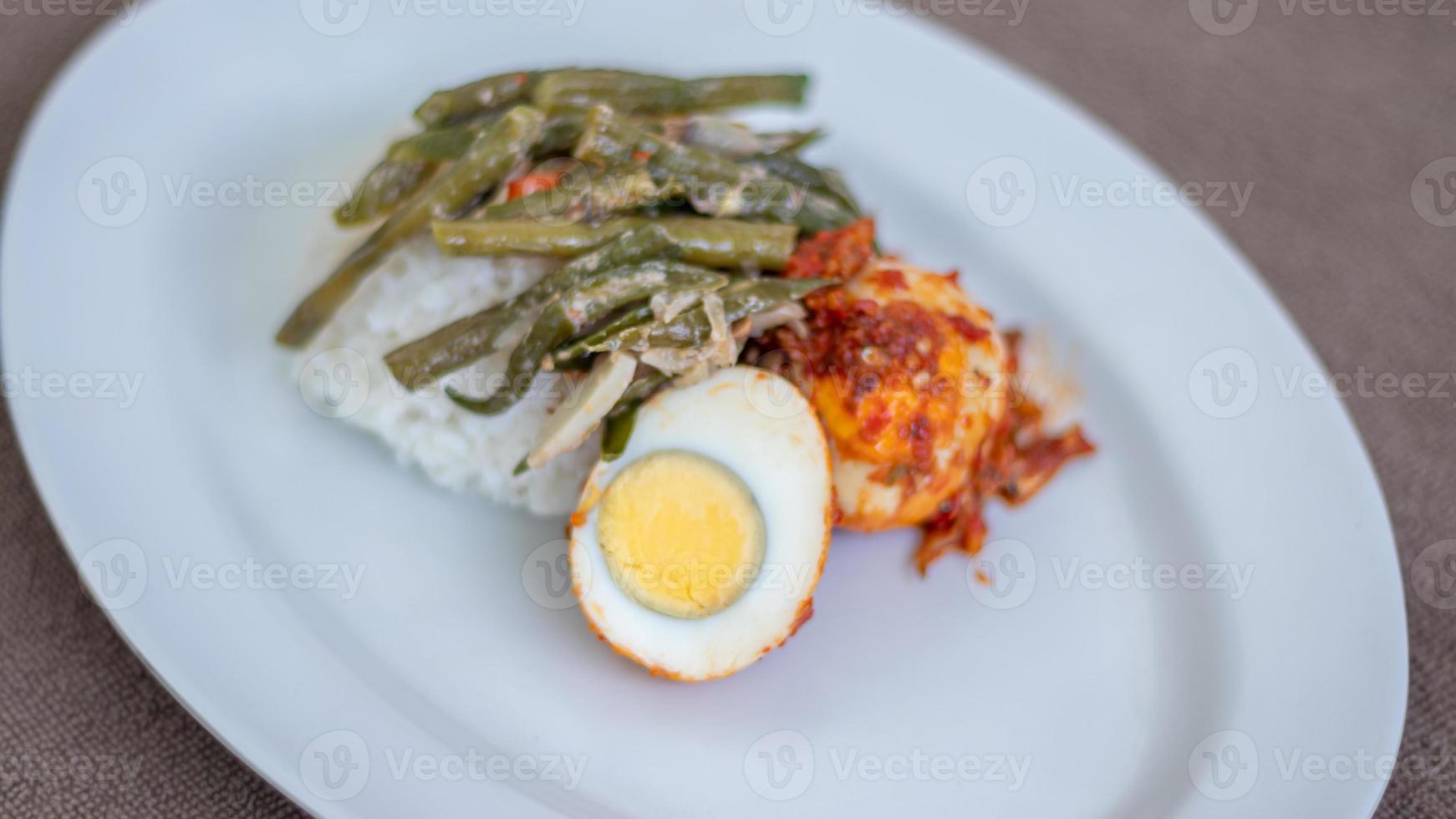en tallrik av ris med ägg balado och lång böna sås, chili sås fylld med ägg, ansjovis och tofu. eras i en skål på en grå bakgrund. vald fokus. foto