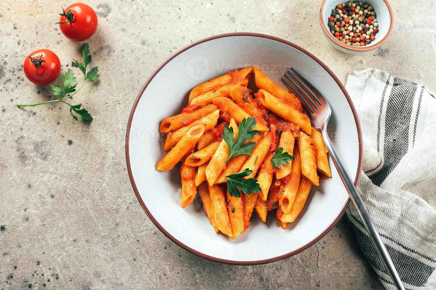 penne pasta med tomat sause i tallrik på sten bakgrund tabell. topp se. italiensk mat foto