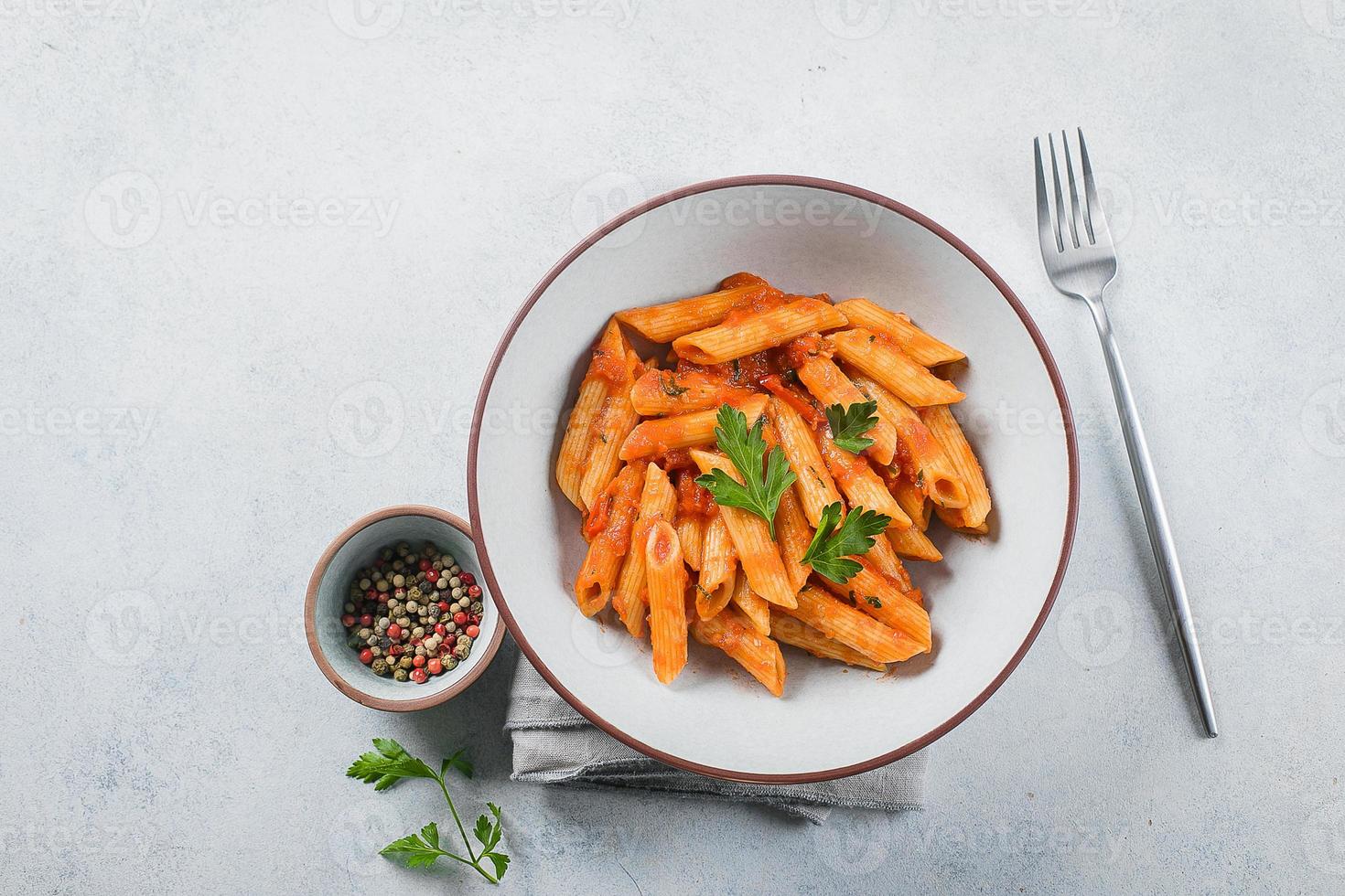 penne kryddad pasta med tomat sause och papper i tallrik på sten bakgrund tabell. topp se. foto