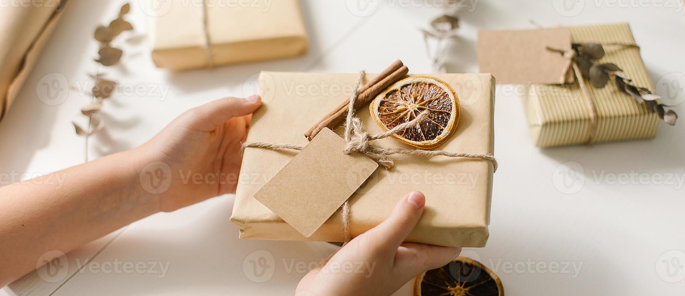 händer innehav eleganta enkel jul gåva i hantverk papper naturlig jul dekorationer. plats för text foto