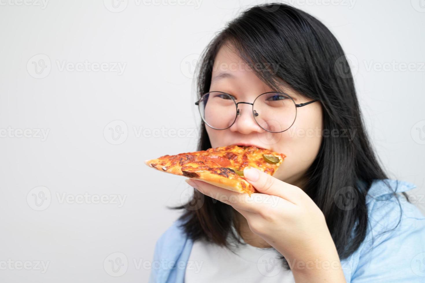 Lycklig glasögon asiatisk ung kvinna äta pizza på vit bakgrund. foto