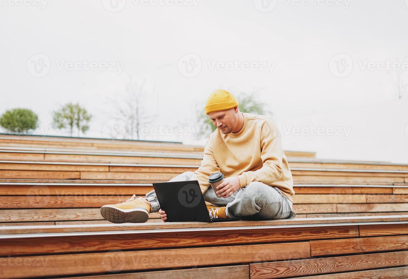 eleganta man hipster i gul hatt frilansare arbetssätt på bärbar dator i de gata stad parkera foto