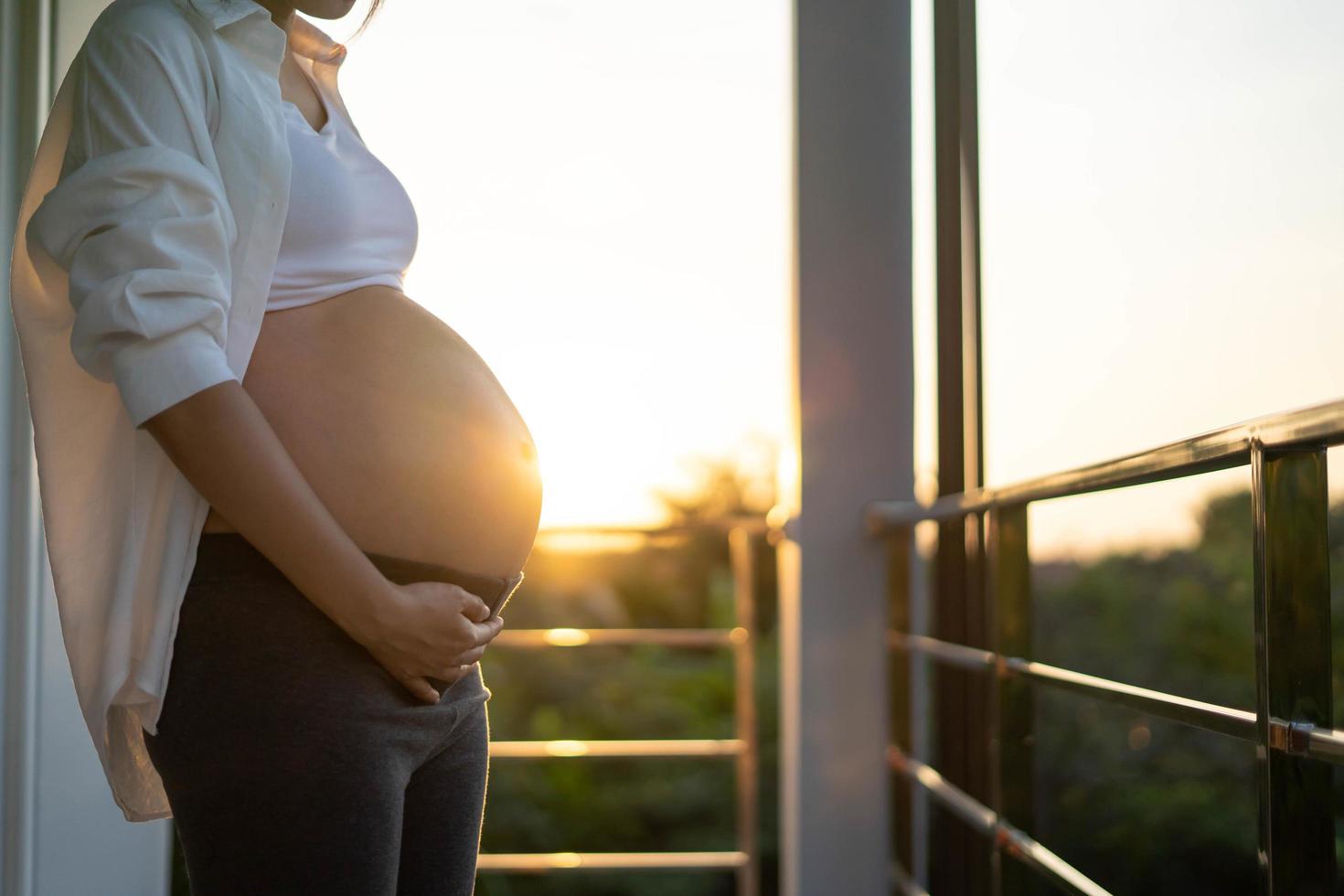 ett 8 månad gravid kvinna försiktigt finputsning henne mage på solnedgång. mamma med bebis i abbomen så Lycklig tid medan hon är gravid. foto