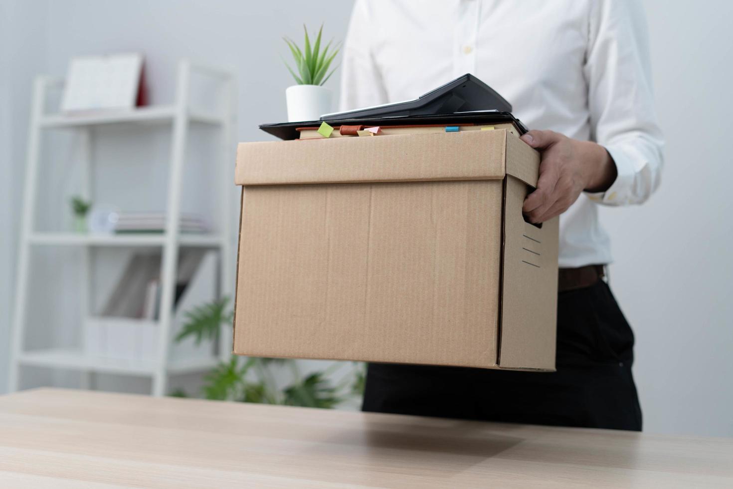 en affärsman innehar en låda för personlig objekt efter sändning en avgång brev till ett verkställande eller chef. inkludera information handla om avgång och lediga platser och jobb ändringar. foto