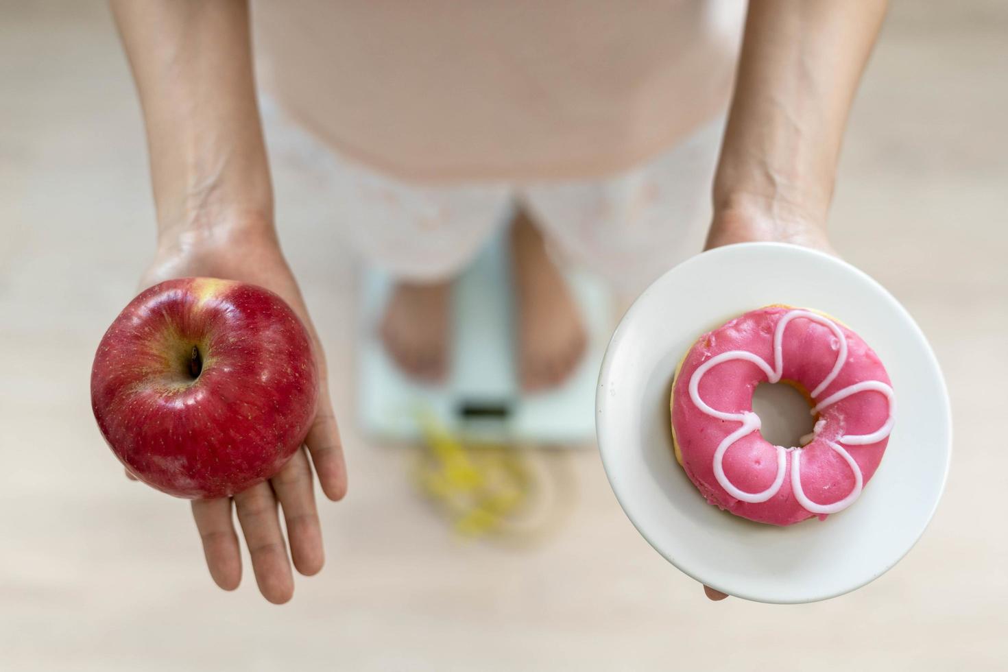 kvinnor är välja de rätt mat för Bra hälsa. kvinnor är fasta. jämförelse alternativ mellan munkar och äpplen under vikt mått på digital vågar. diet begrepp. foto