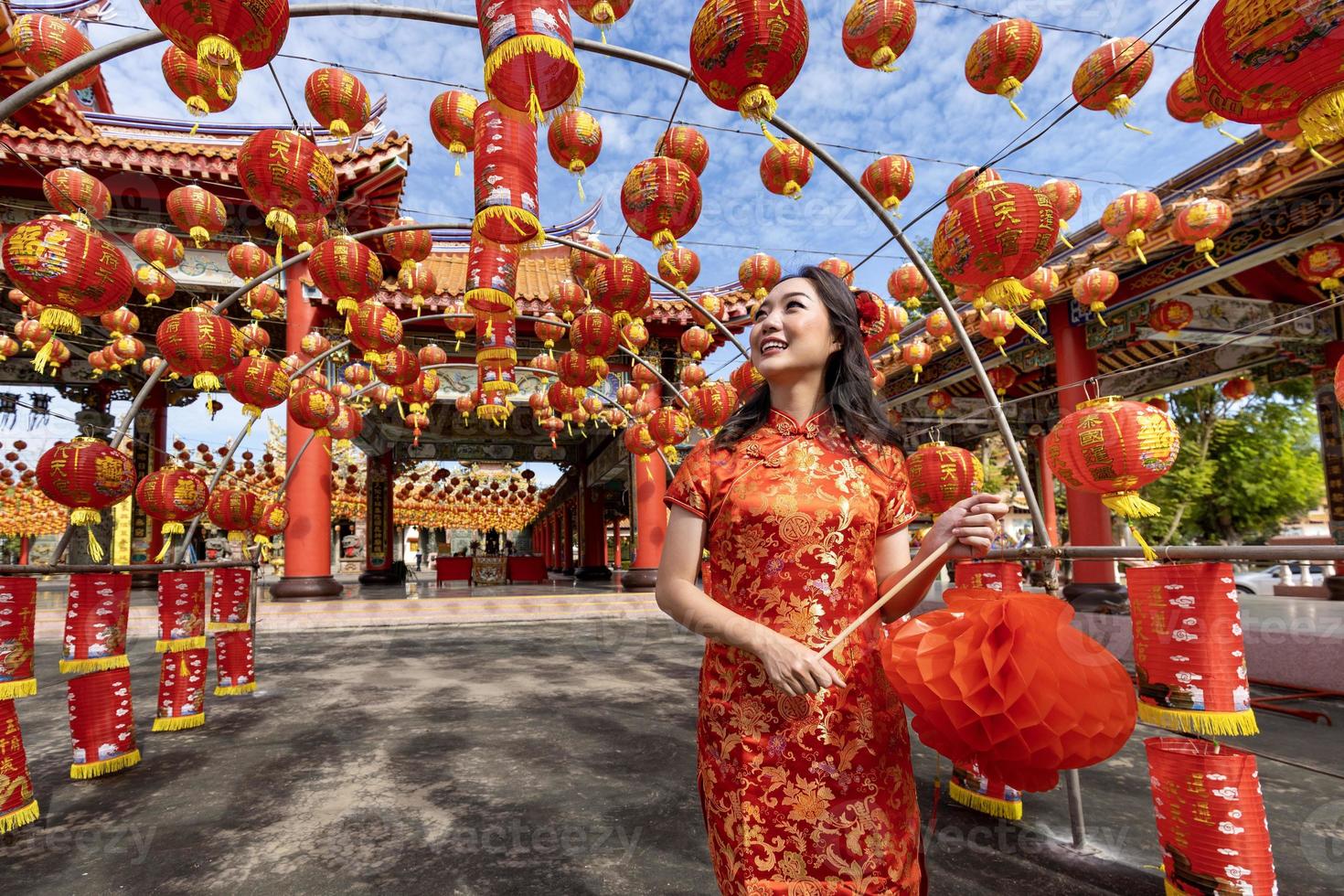 asiatisk kvinna i röd Cheongsam qipao klänning innehav lykta medan besöker de kinesisk buddist tempel under lunar ny år för traditionell kultur begrepp foto