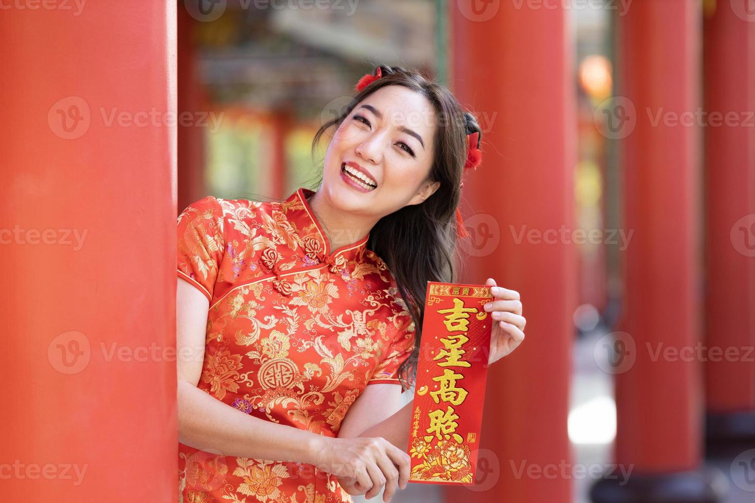 asiatisk kvinna i röd Cheongsam qipao klänning är innehav välsignelse förmögenhet kort ordspråk till vara välsignad förbi en tur- stjärna inuti kinesisk buddist tempel under lunar ny år för bäst önskar och Bra tur begrepp foto