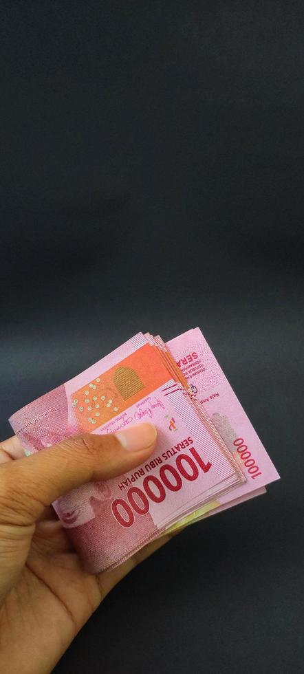 porträtt av indonesiska sedlar rp. 100 000 i hand. indonesiska rupiah valuta isolerat på svart bakgrund foto