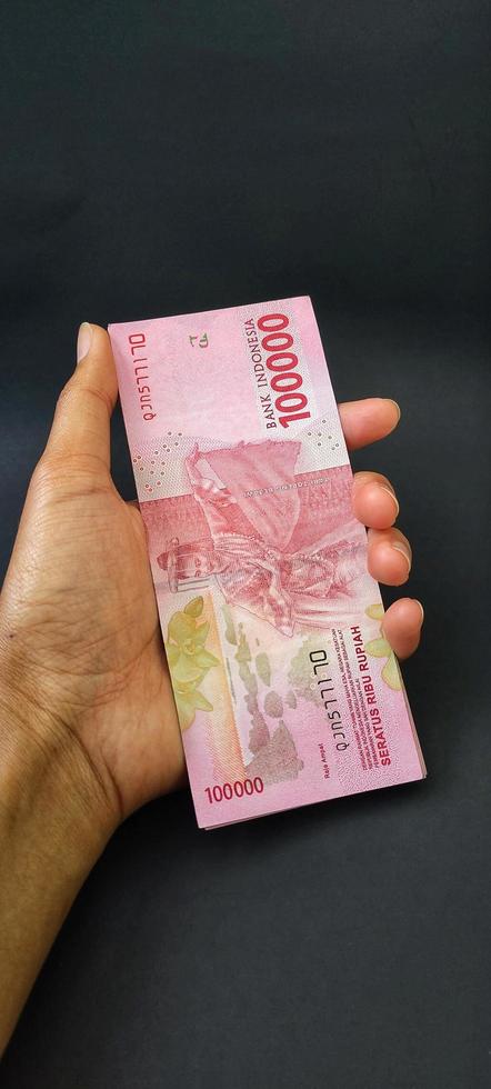 porträtt av indonesiska sedlar rp. 100 000 i hand. indonesiska rupiah valuta isolerat på svart bakgrund foto