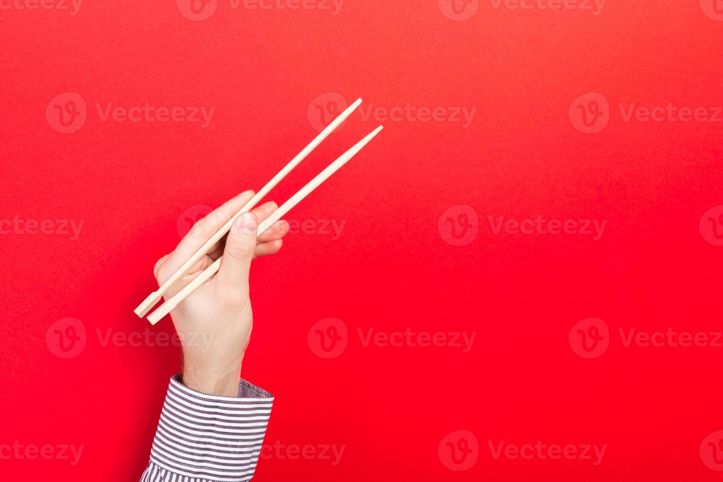 manlig hand med ätpinnar på röd bakgrund. traditionell asiatisk mat med emty Plats för din design foto