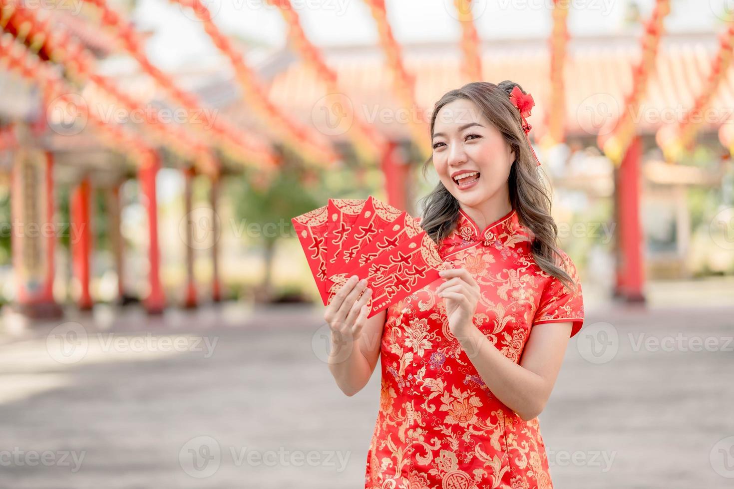 porträtt skön asiatisk kvinna bär traditionell Cheongsam qipao kostym innehav ang pao, röd kuvert i kinesisk buddist tempel. fira kinesisk lunar ny år, festlig säsong Semester. foto