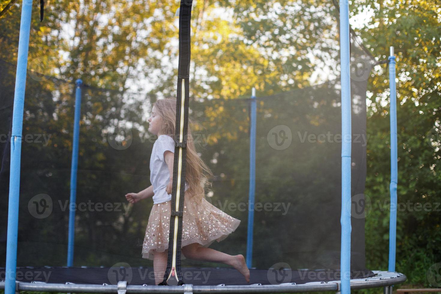 liten barn flicka Hoppar på de trampolin i de tillbaka gård foto