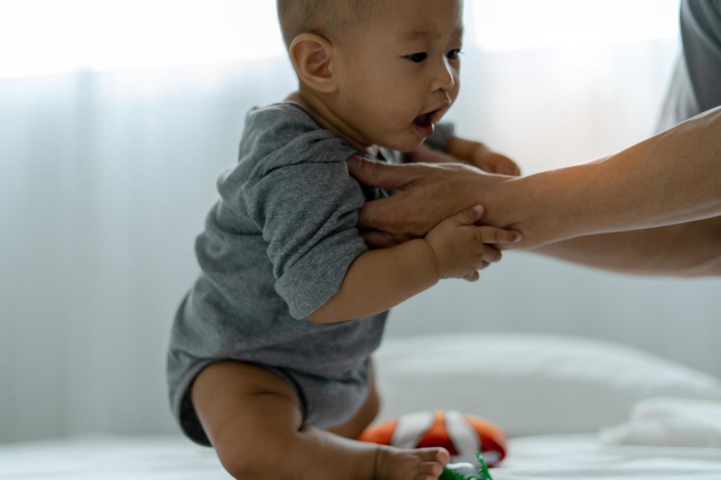 spädbarn asiatiska. ett asiatisk bebis litar på hans fars hand till stå upp. far och son utgifterna tid tillsammans foto