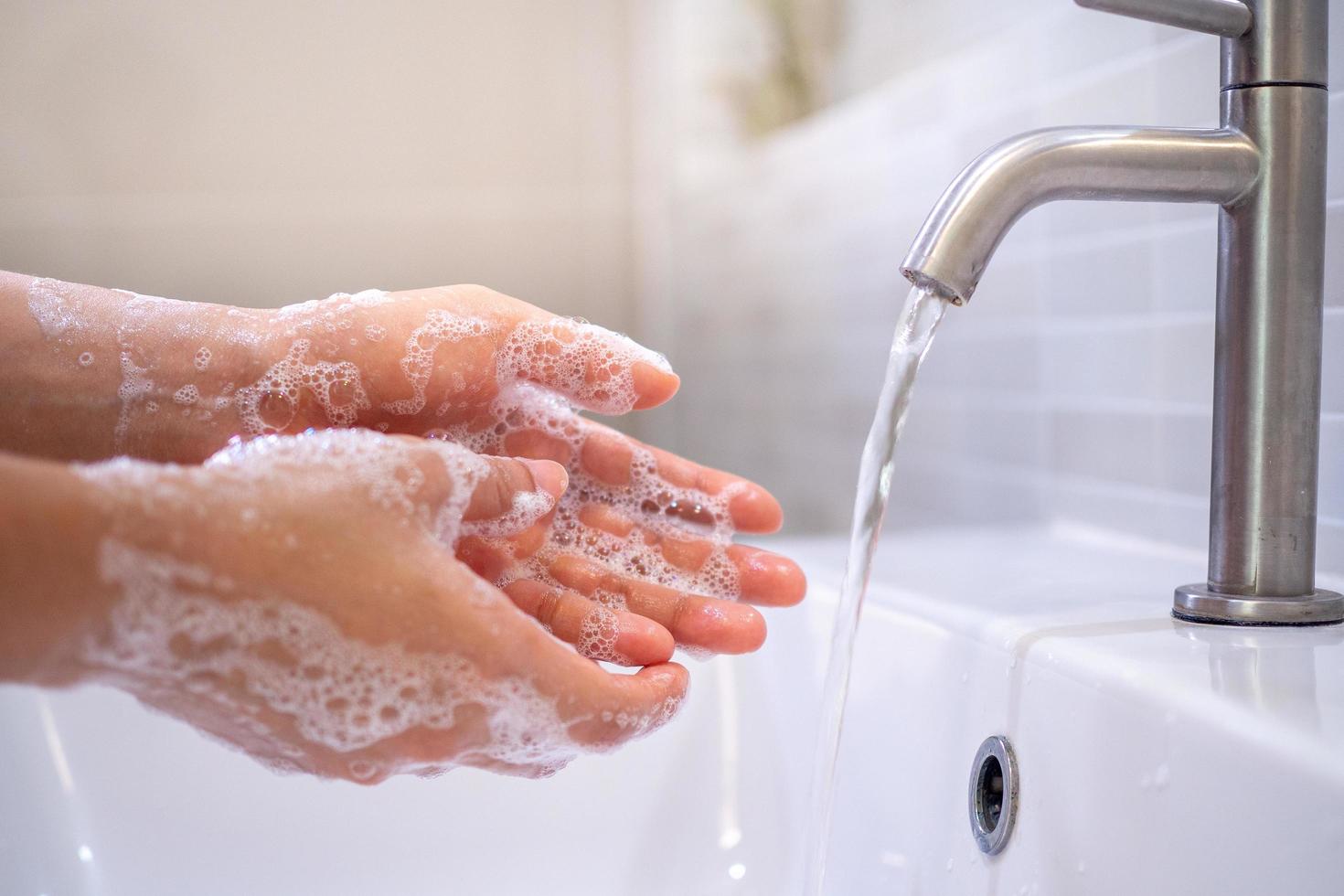 en stänga upp av en ung kvinnas hand tvättning händer med tvål gel i de badrum handfat hand rengöring till förhindra de spridning av de covid19 virus. hälsa vård begrepp foto