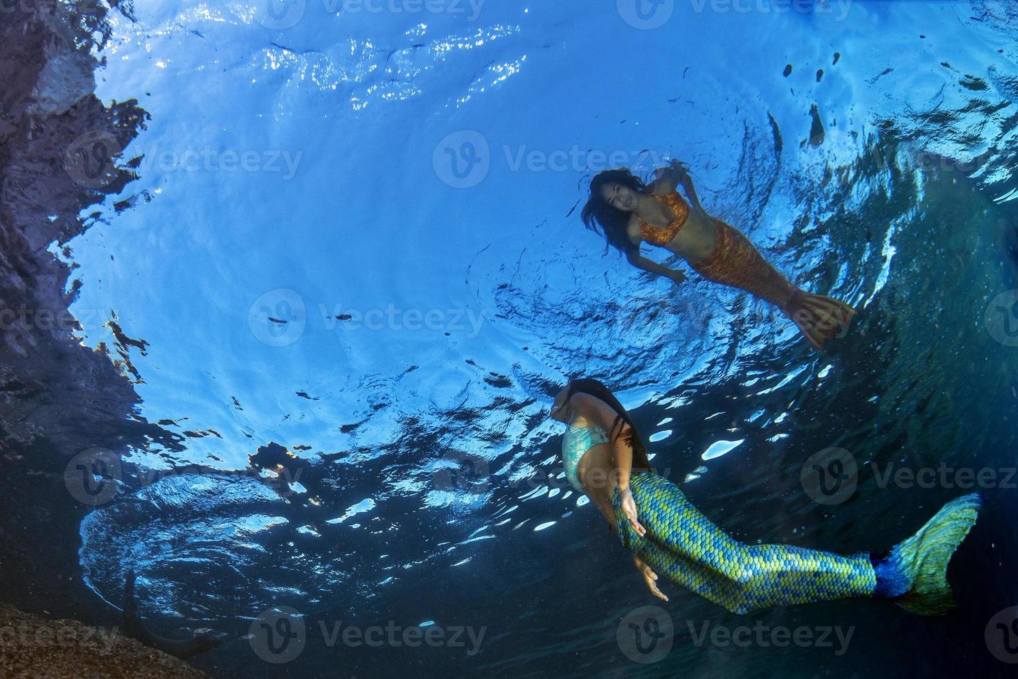 två sjöjungfru simning under vattnet i de djup blå hav foto