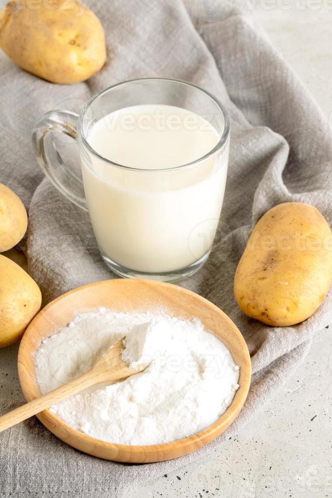 glas kopp med potatis mjölk, potatis pulver i trä- tallrik och knölar på grå servett på betong. foto