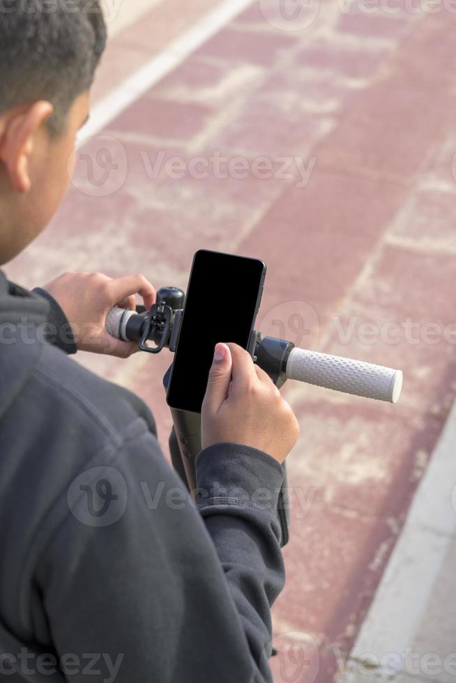 ung man på ett elektrisk skoter använder sig av smartphone gps tillämpningar foto