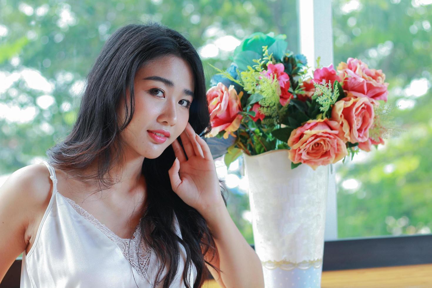 asiatisk kvinna som sitter bredvid en vas med blommor foto