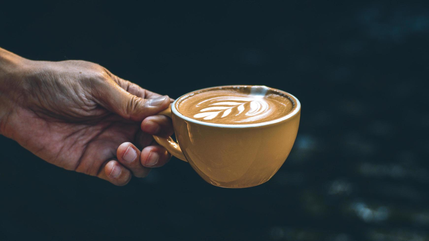 hand som håller en latte i en gul mugg foto