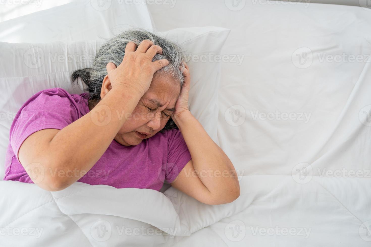 senior kvinna med grå hår i säng känna deprimerad eller lidande från stark huvudvärk migrän och hög blod tryck, sömnlös person påfrestande till sömn störd kasta och sväng i sovrum foto