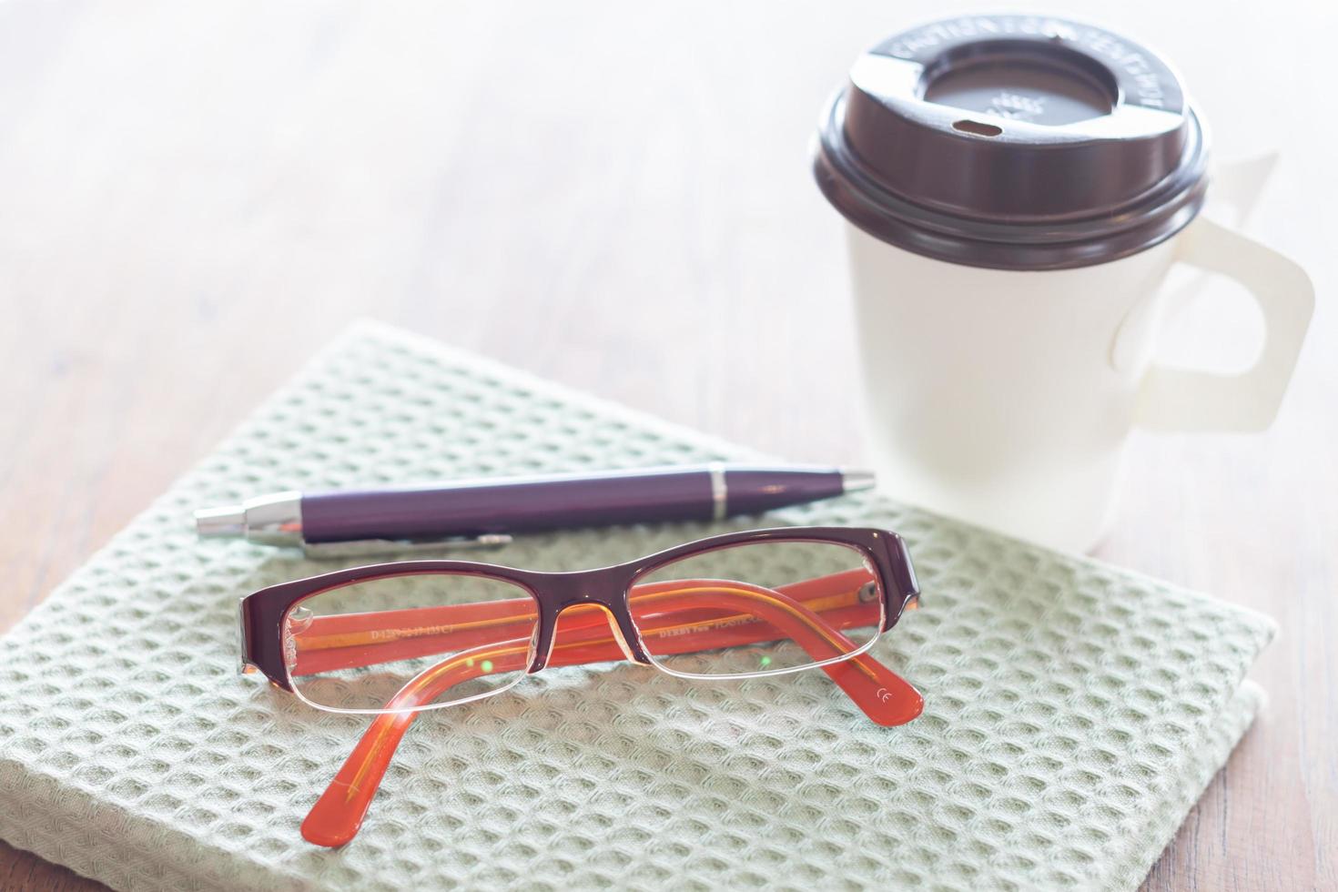 anteckningsbok, penna, glasögon och en kaffekopp på ett träbord foto