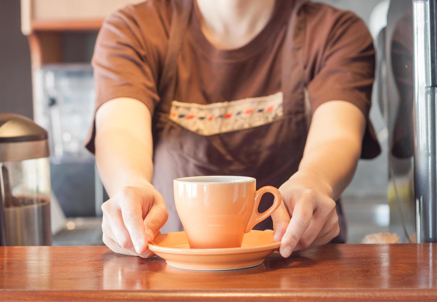 barista som erbjuder orange kopp kaffe foto