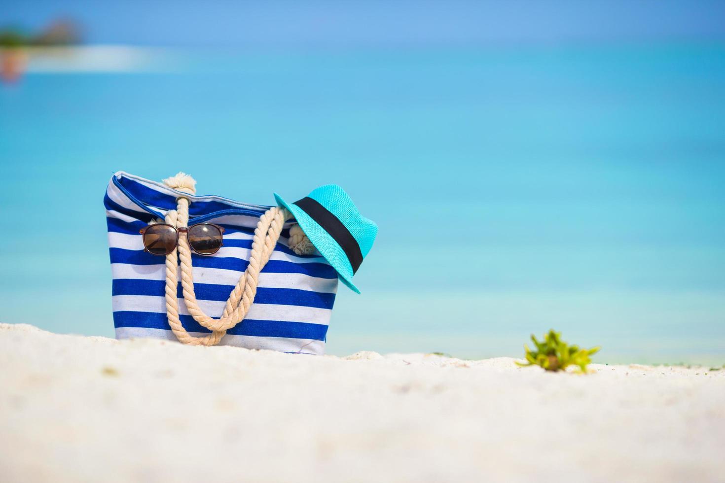 väska med solglasögon och hatt på en strand foto