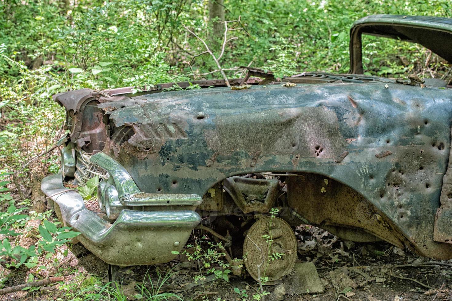 gammal rostig bil övergiven i skog med pistol kula hål foto