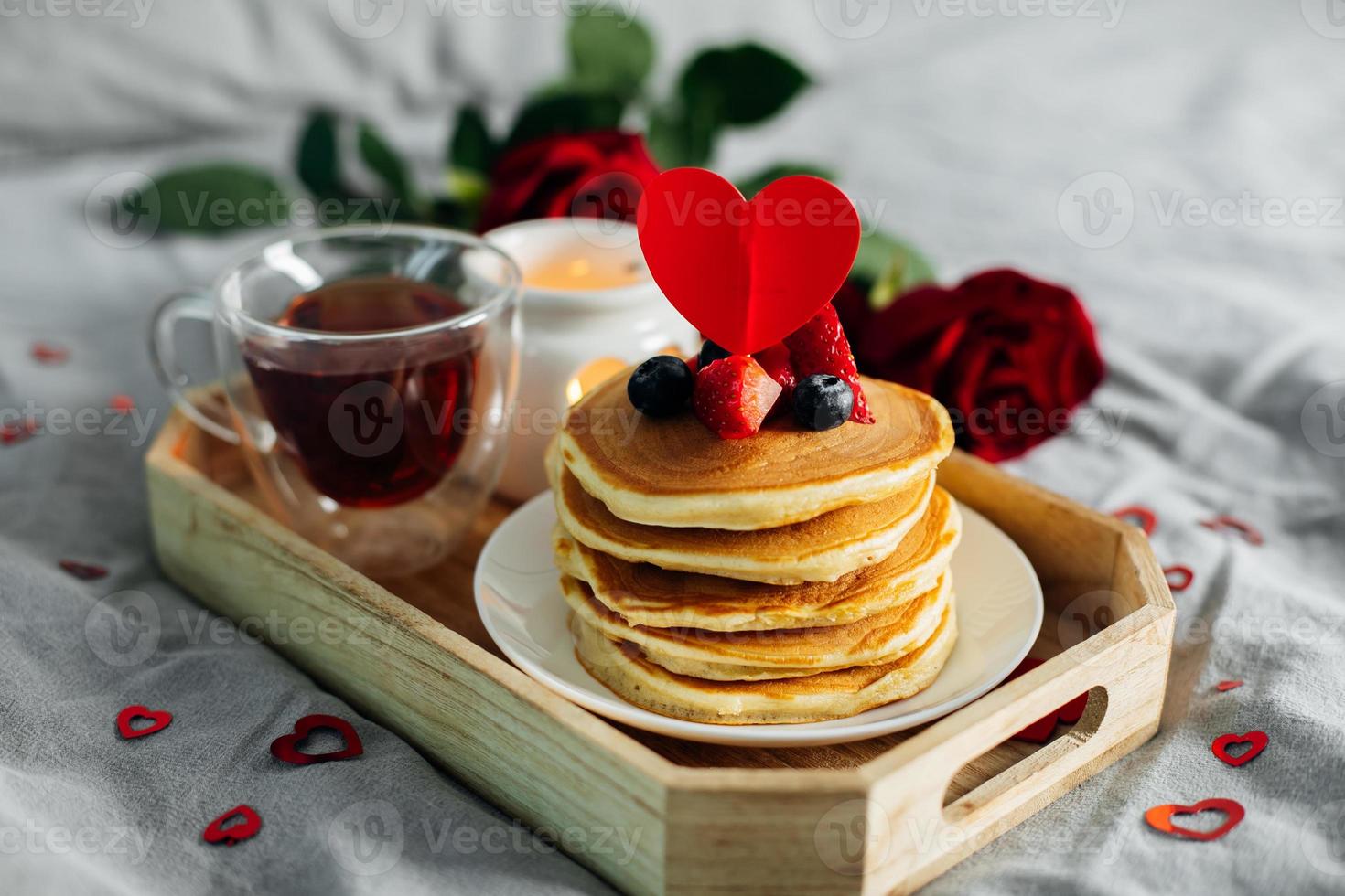 hemlagad pannkakor med bär, kopp av te och blommor och gåva låda. frukost eller brunch för hjärtans dag. foto