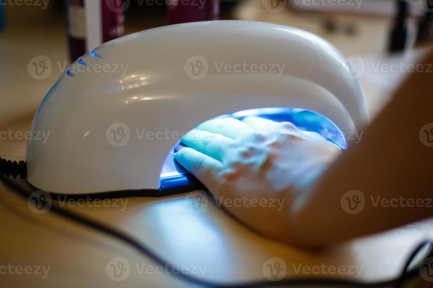 närbild av de hand av en kvinna inuti en uv lampa härdning henne nyligen applicerad gel nagel putsa foto