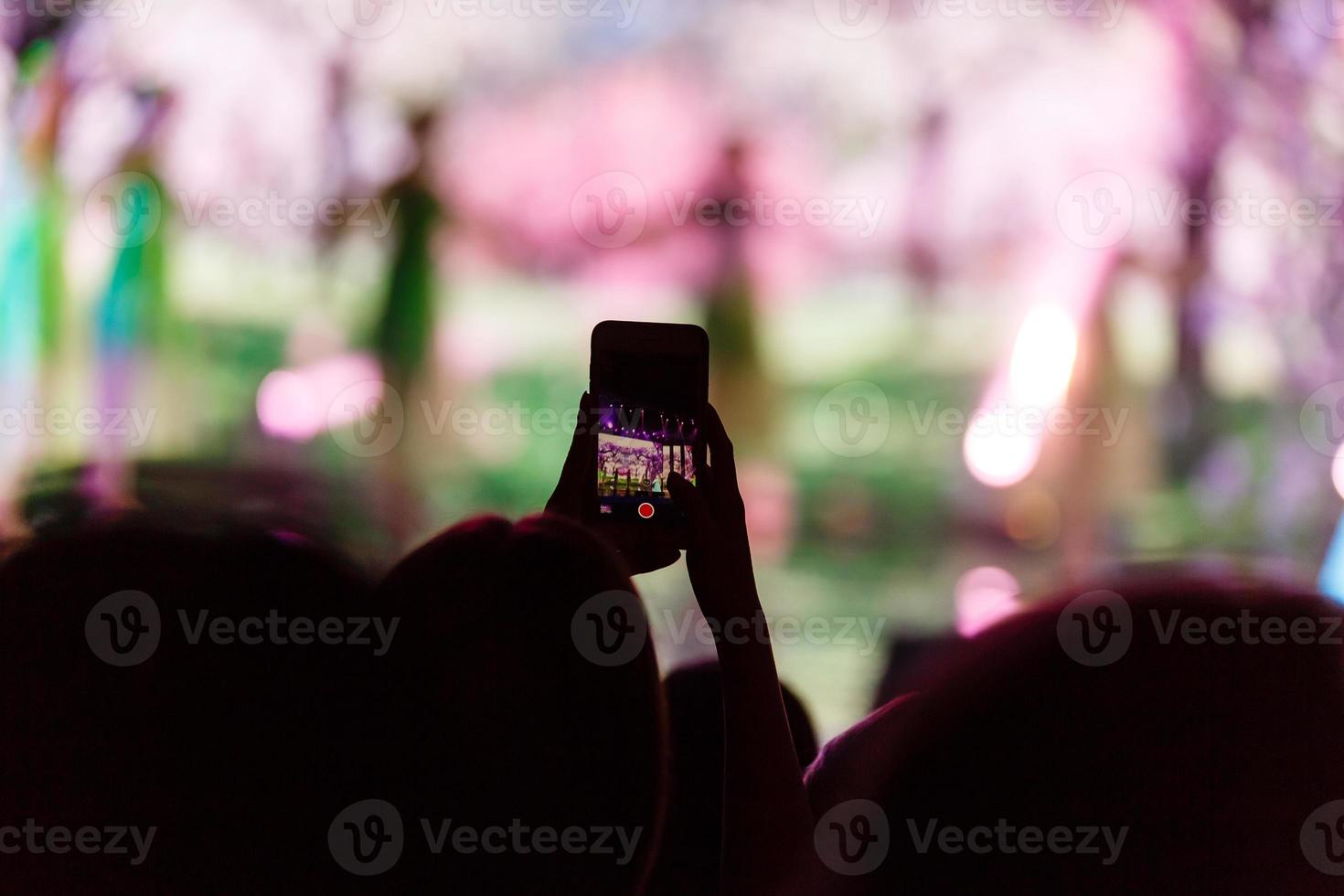 en smartphone hölls med två hand i beställa till skjuta en antal fot under en konsert. foto