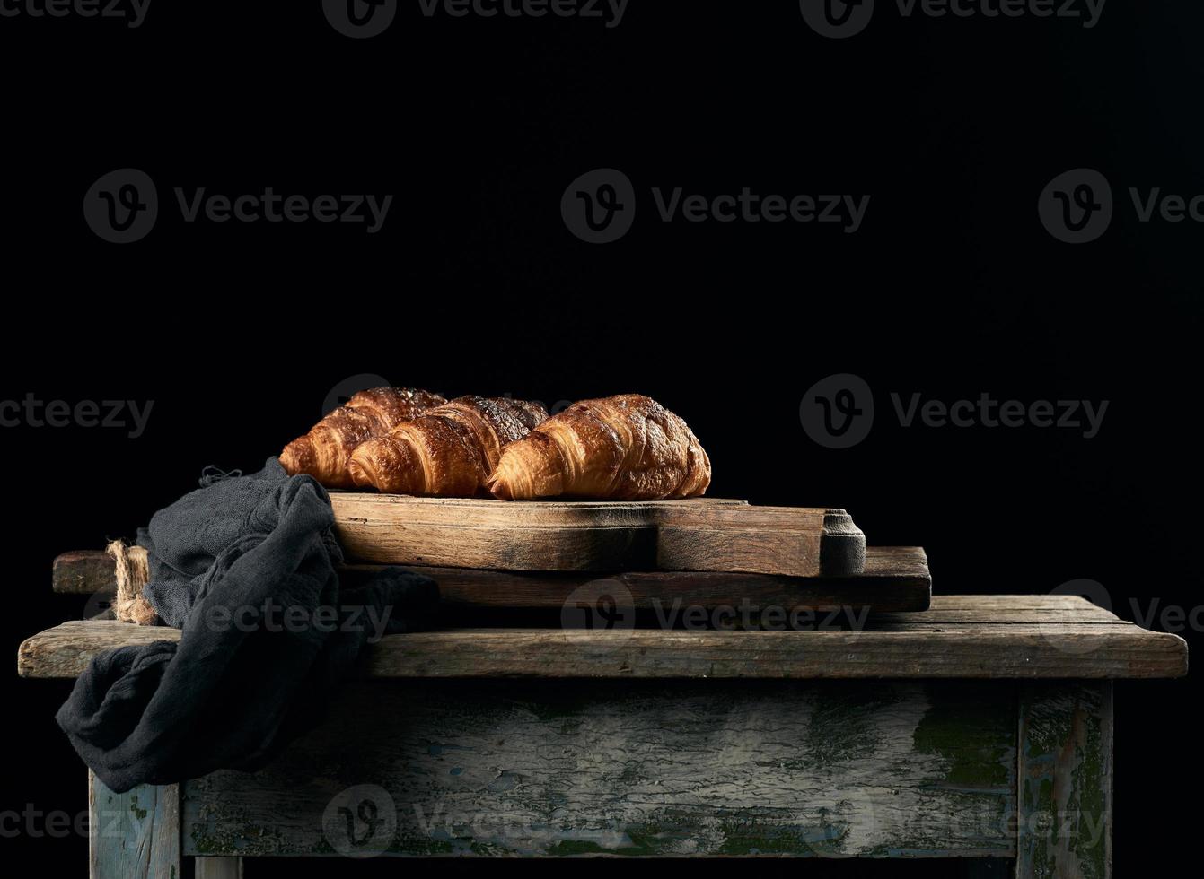 bakad croissanter på brun kök styrelse, svart bakgrund foto