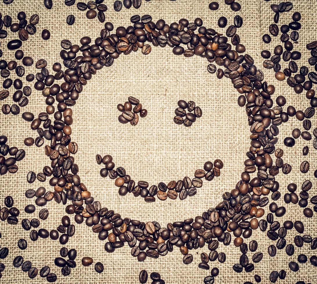 leende ansikte bildas förbi kaffe korn på en grov trasa omgiven förbi kaffe bönor foto