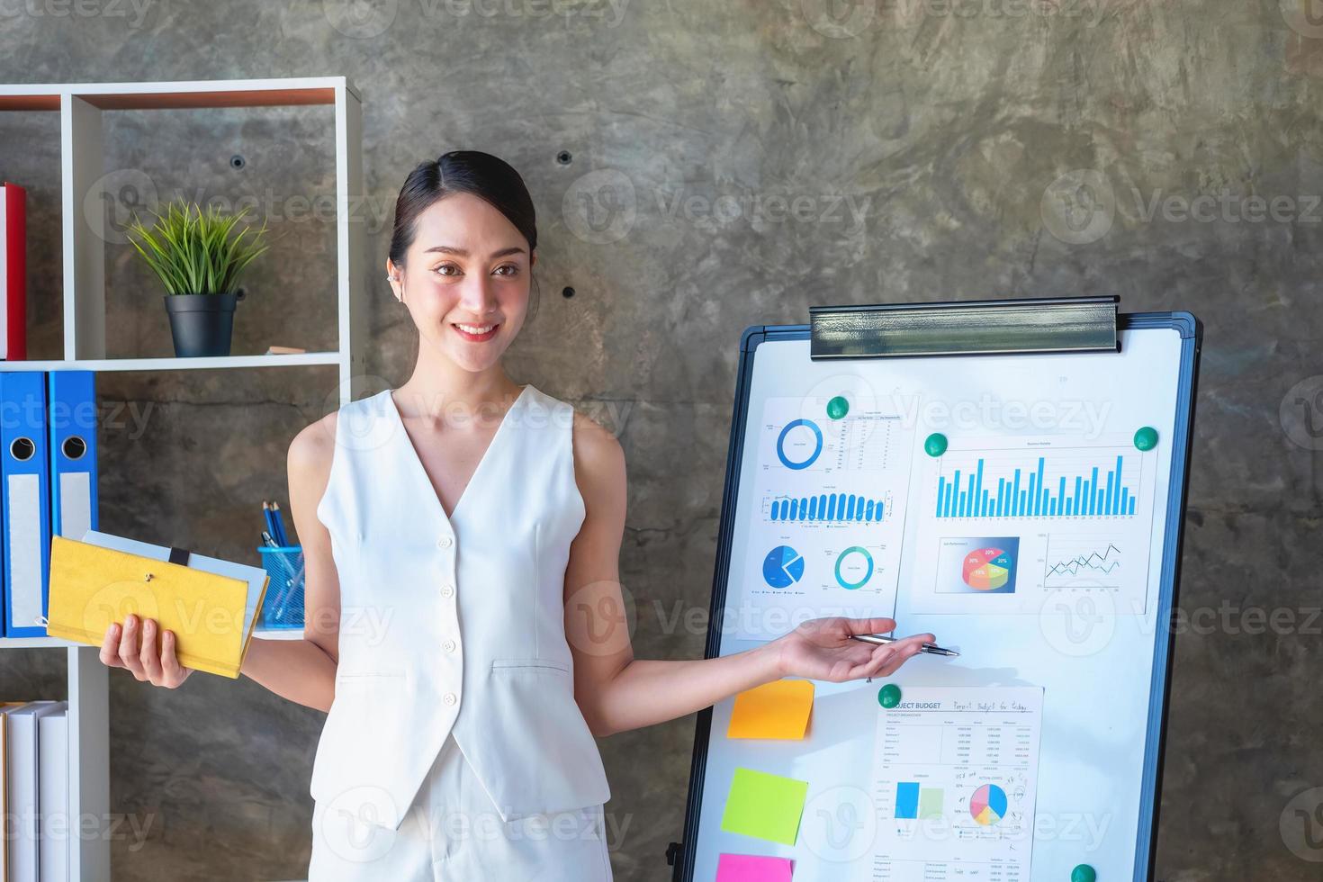 asiatisk affärskvinna presenter företag data med en styrelse med diagram, grafer hand innehav en gul anteckningsbok, och företag dokument liggande på de tabell i de kontor, företag begrepp. foto