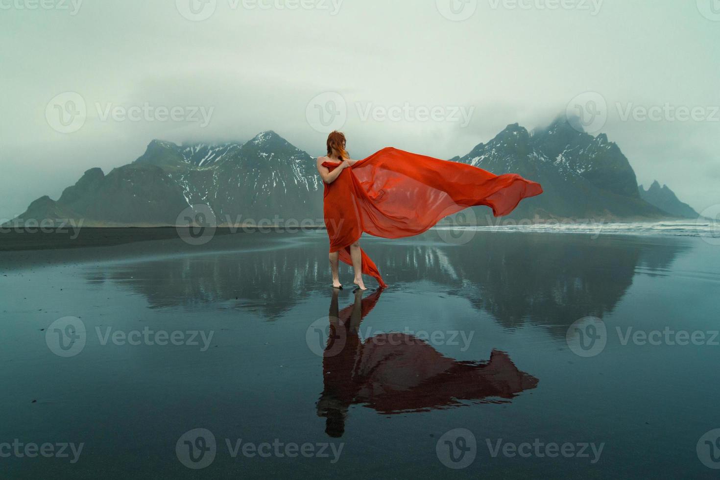 kvinna i röd klänning med vinka cape på strand naturskön fotografi foto