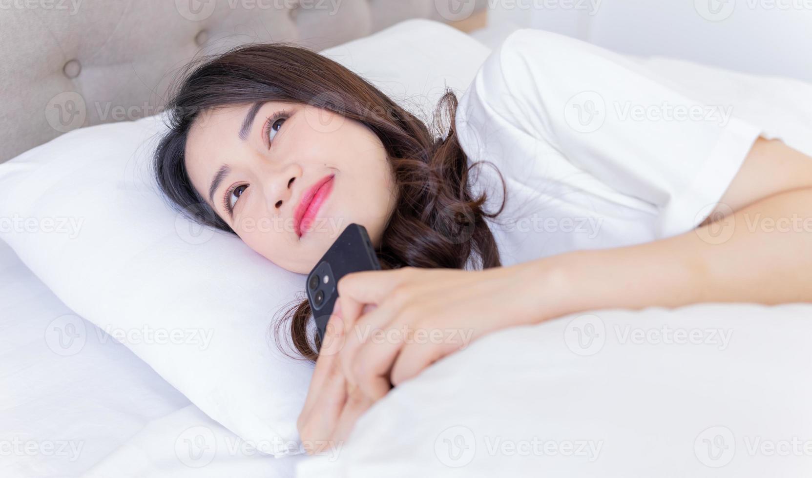 ung asiatisk kvinna använder sig av smartphone på säng foto