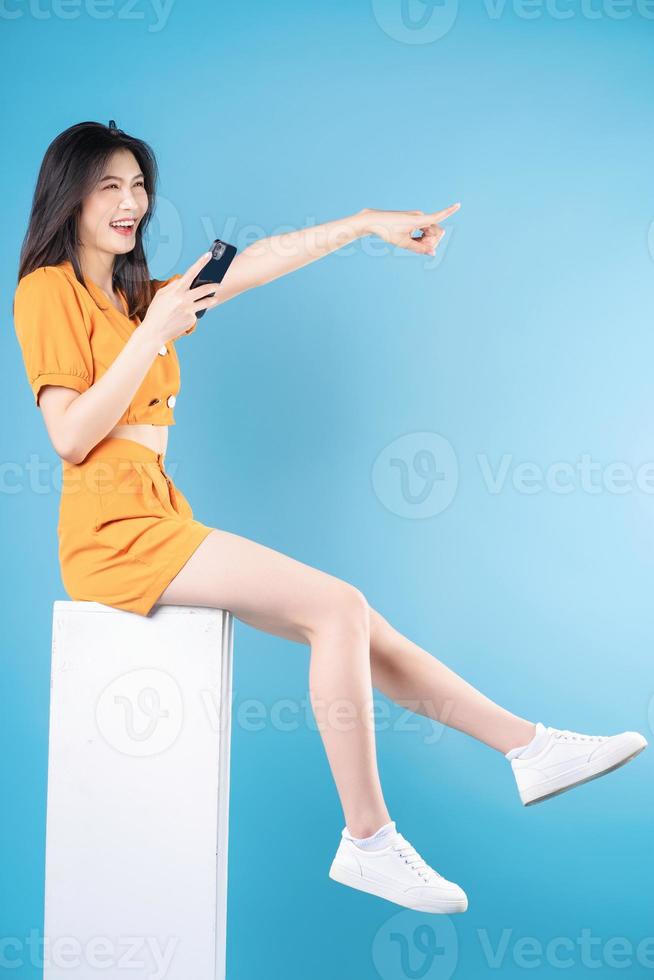 full längd Foto av ung asiatisk kvinna använder sig av smartphone på blå bakgrund